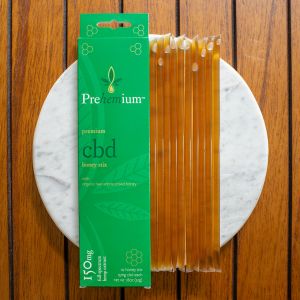 Prehemium premium cbd honey sticks - 15mg. Image of packaging next to 10 honey sticks on a white marble slab.